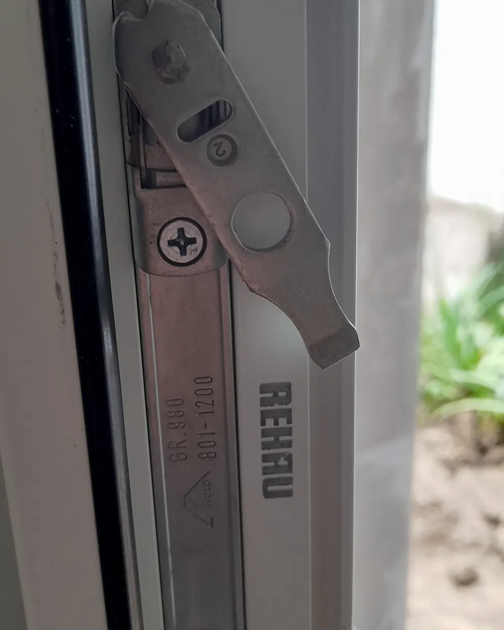 El herraje de una ventana de PVC blanca, con la marca REHAU en el perfil