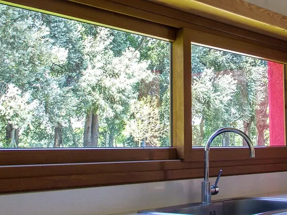 Ventana de PVC roble dorado sobre la mesada de la cocina, con los árboles afuera