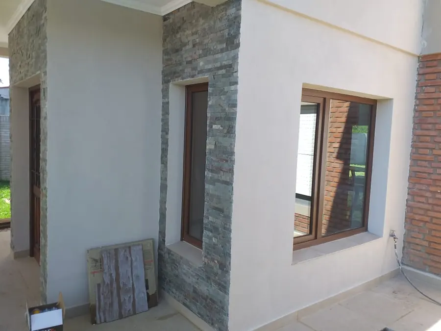 Frente de piedra y revoque con ventanas de PVC roble