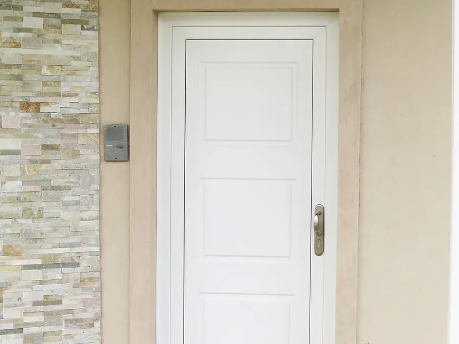 Puerta de entrada de PVC blanco junto a un revestimiento de piedra