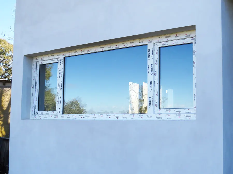 Ventana de PVC blanco con paño fijo, en una pared celeste