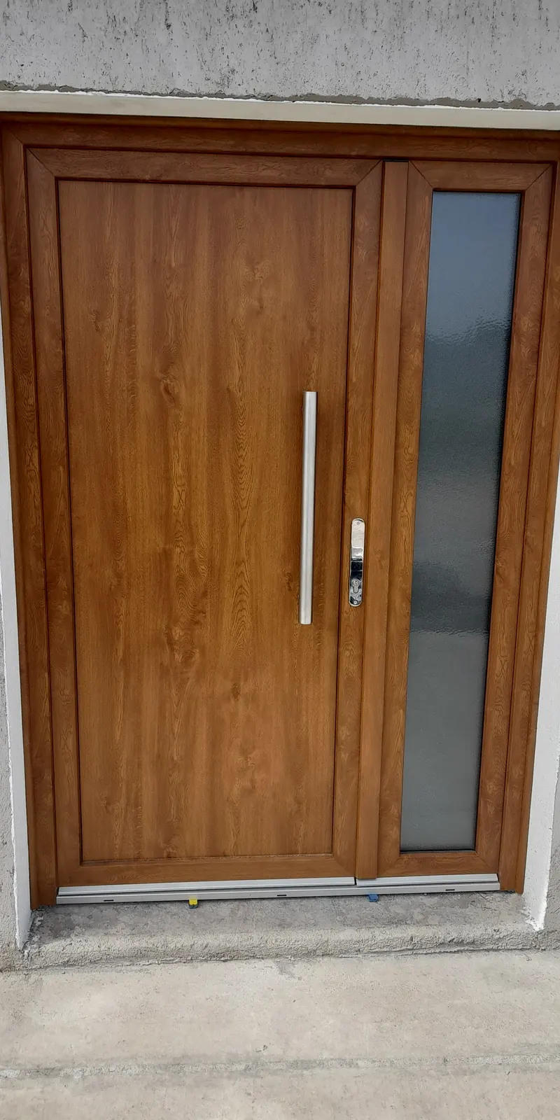 Puerta de entrada de PVC color roble con un paño lateral de vidrio, ya colocada
