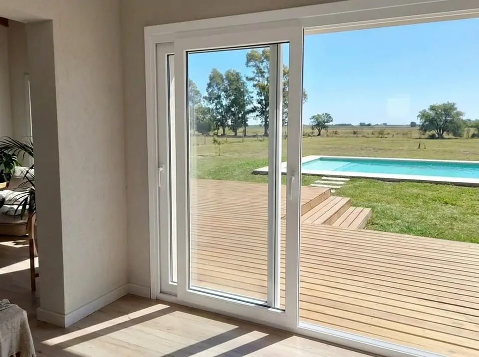 Puerta balcón corrediza de PVC blanco, abierta al deck y la pileta